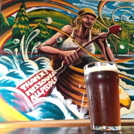 ale posed next to a rafting mural in Missoula brewery