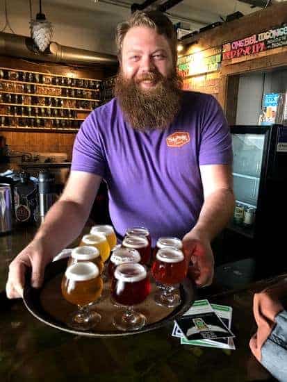 Tyler, beeldender at Strange Craft Beer Company in Denver holding a tray of beers