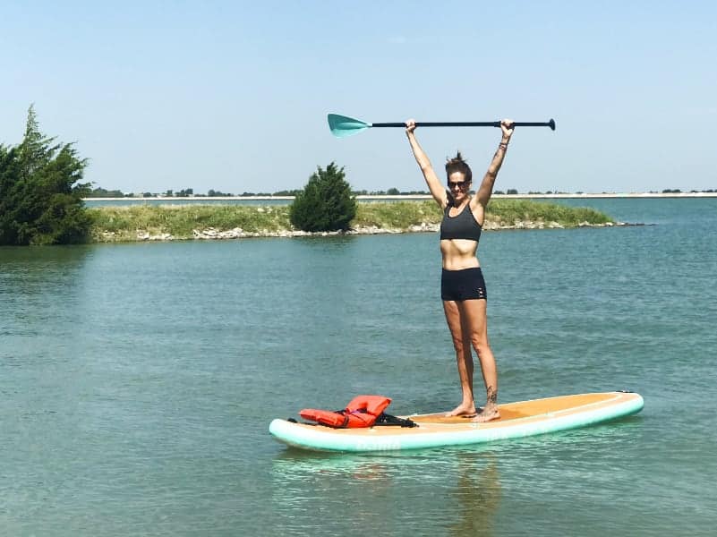 woman on Paddleboard in lake holding up paddle